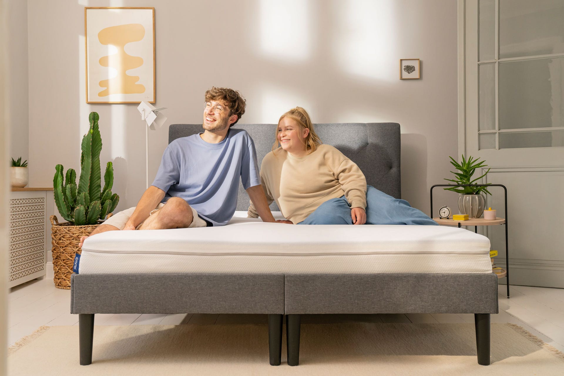 Junges Paar sitzt entspannt auf Emma Boxspringbett in sonnigem Zimmer.